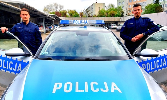 Dwóch policjantów stojących przy radiowozie.