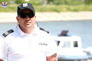 policjant pełniący służbę nad Zalewem Zemborzyskim, w tle łódź policyjna