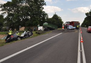 fot. miejsce wypadku drogowego, rozbity volkswagen, w tle przyczepa i ciągnik rolniczy, policjanci, strażacy i ratownicy oraz wóz strażacki