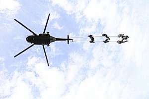 Zdjęcie wykonane pod śmigłowcem w czasie jego lotu. Na linie zamocowana jest grupa funkcjonariuszy wiszą oni pod śmigłowcem.