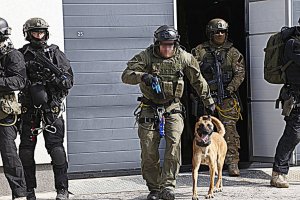 Funkcjonariusze samodzielnego pododdziału kontrterrorystycznego Policji z wykorzystaniem psa szturmowego wychodzą z budynku.
