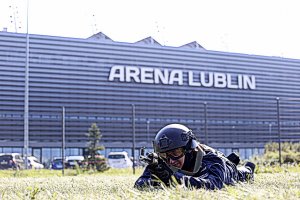 Policjant leży na ziemi z AK 47 za nim stadion Arena Lublin