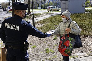 Policjant podaje starszej kobiecie maseczkę ochronną.