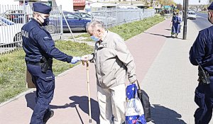 Policjant w mundurze przekazuje starszemu mężczyźnie maseczkę ochronną.
