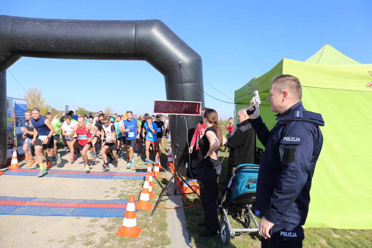 komendant daje sygnał do startu w tle widać start i uczestników biegu