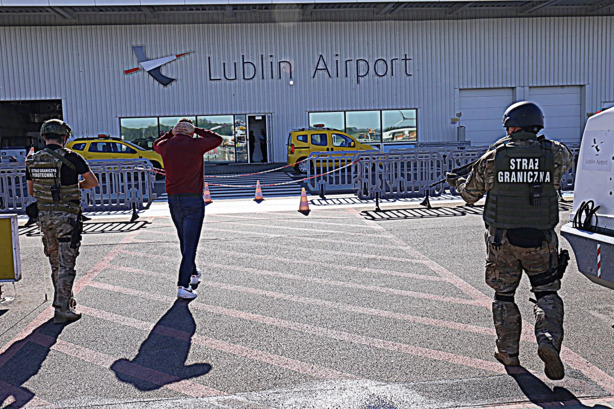 Straż Graniczna prowadzi zakładnika po płycie lotniska.