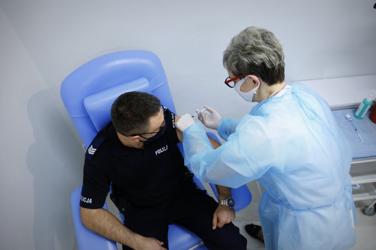 Zdjęcie zrobione z góry policjant otrzymuje szczepionkę od pielęgniarki.