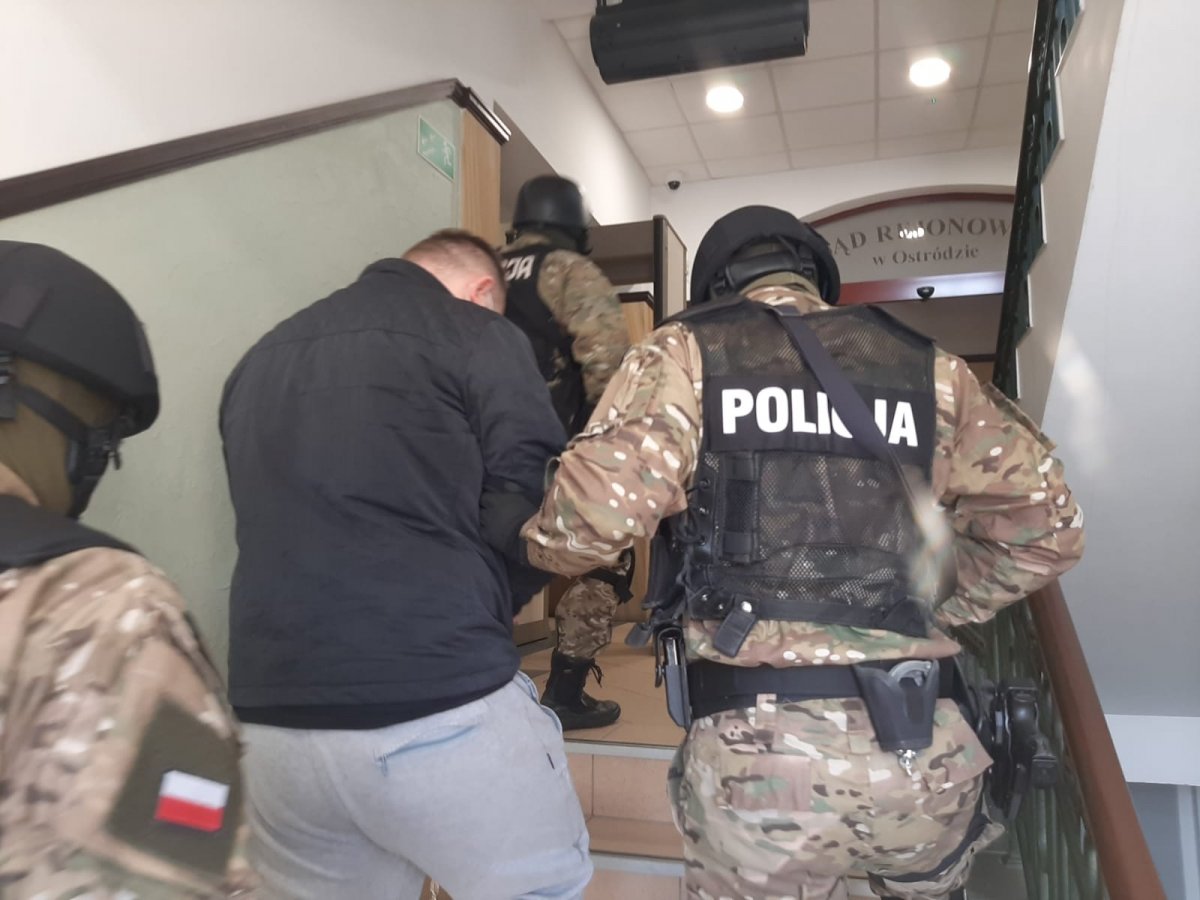 Policjanci w sąszie w Ostrudzie po schodach prowadzą zatrzymanego.