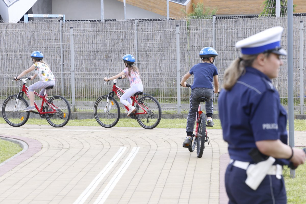 Dzieci jadą na rowerach obok przygląda się policjantka.