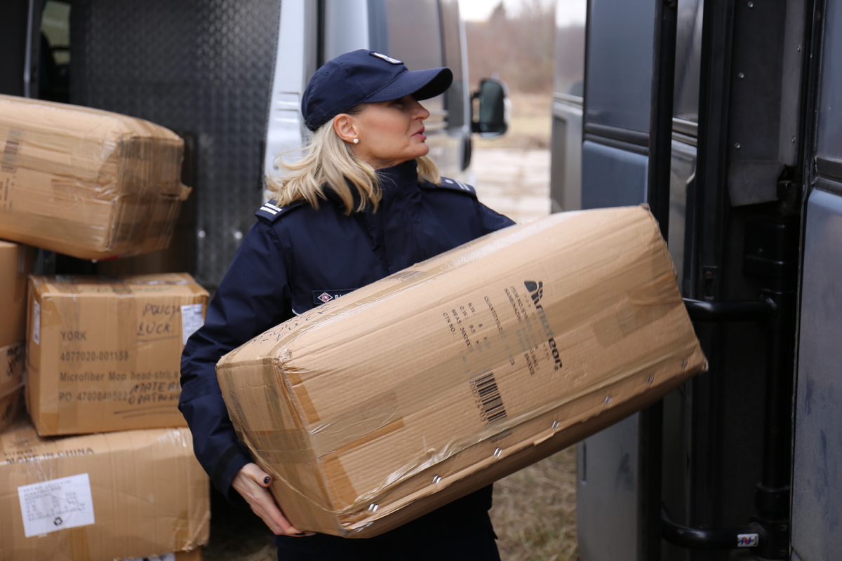 Policjantka niesie pudełko z darami do autokaru.