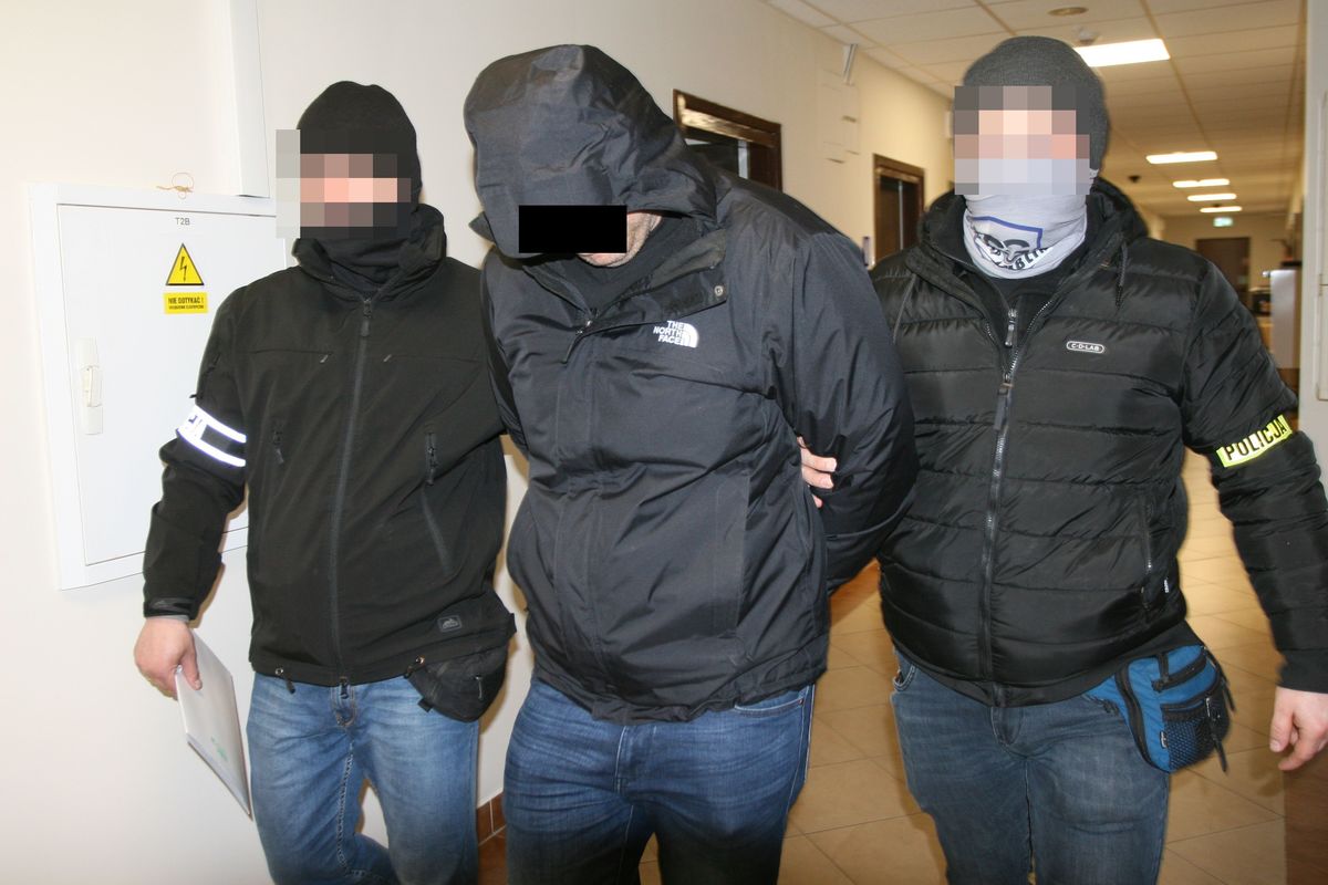 Policjanci prowadzą zatrzymanego mężczyznę w Komendzie Wojewódzkiej Policji w Lublinie.