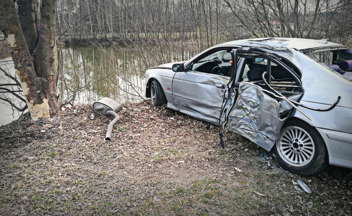 Zdjęcie przedstawia rozbity o drzewo samochód marki BMW koloru srebrnego.