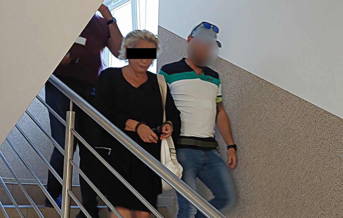 Policjanci prowadzą zatrzymaną kobietę która ma założone kajdanki na ręce trzymane z przodu.