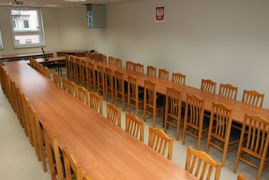 Sala odpraw wyposażona w długie stoły i krzesła.