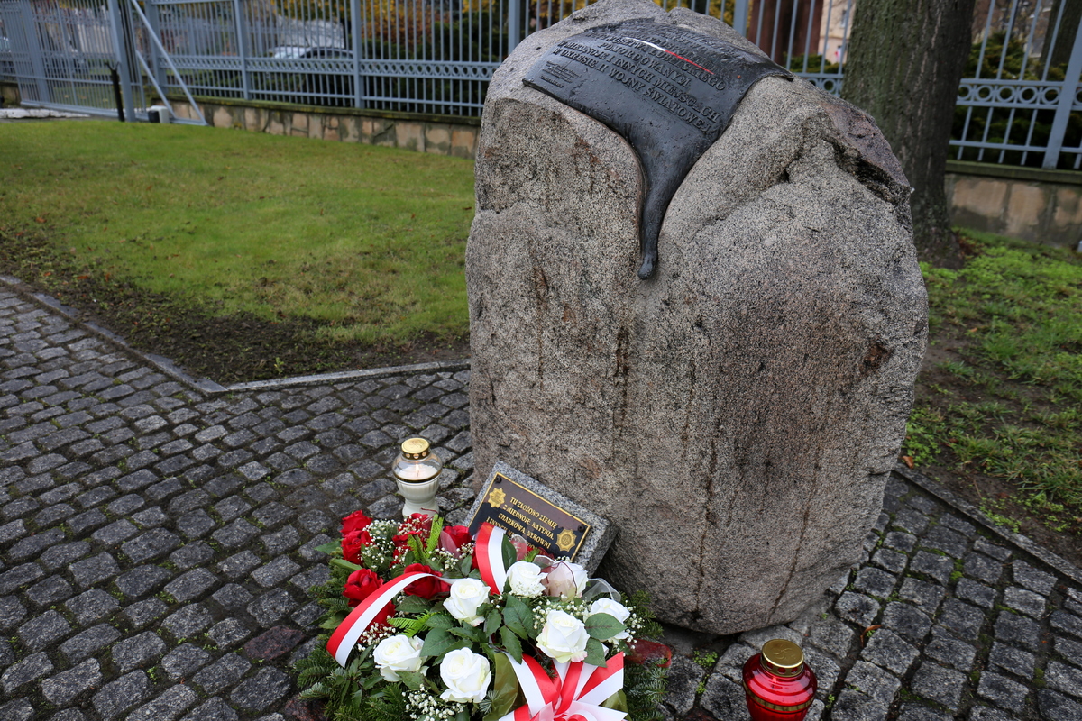 pomnik, przed nim lężą kwiaty i palą się znicze