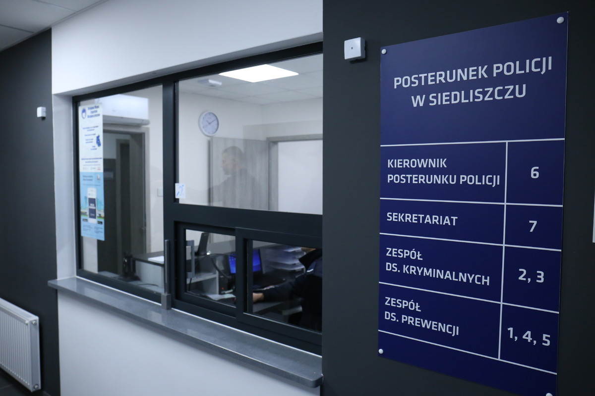 Na zdjęciu widzimy wnętrze budynku, gdzie na scianie jest zamocowana tablica z napisem Posterunek Policji w Siedliszczu oraz numery pomieszczeń z opisem kto się w nich znajduje.