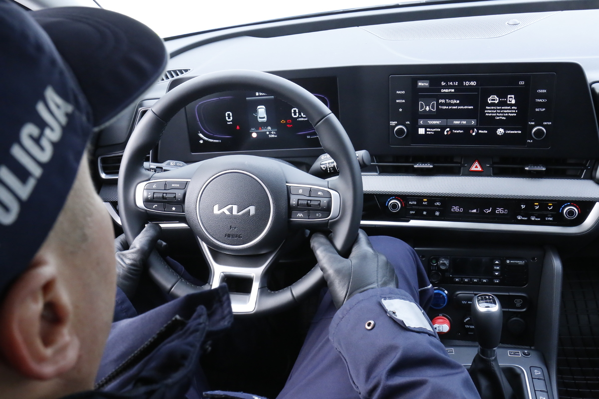 Umundurowany policjant siedzi za kierownicą nowego radiowozu marki Kia Sportage.