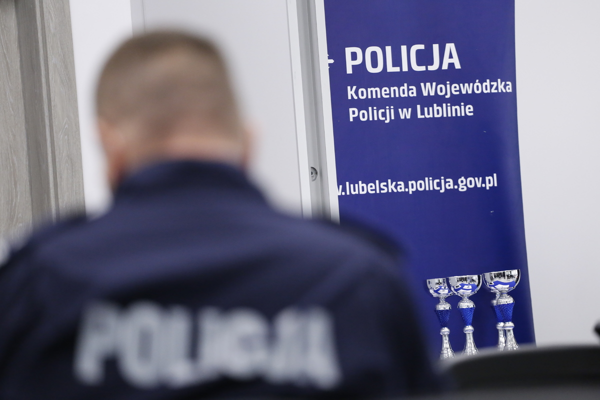 Po lewej stronie zdjęcia widzymy umundurowanego policjanta. W głębi zjęcia po prawej stronie widzimy stojące puchary oraz rolap z napisem Komenda Wojewódzka Policji w Lublinie 