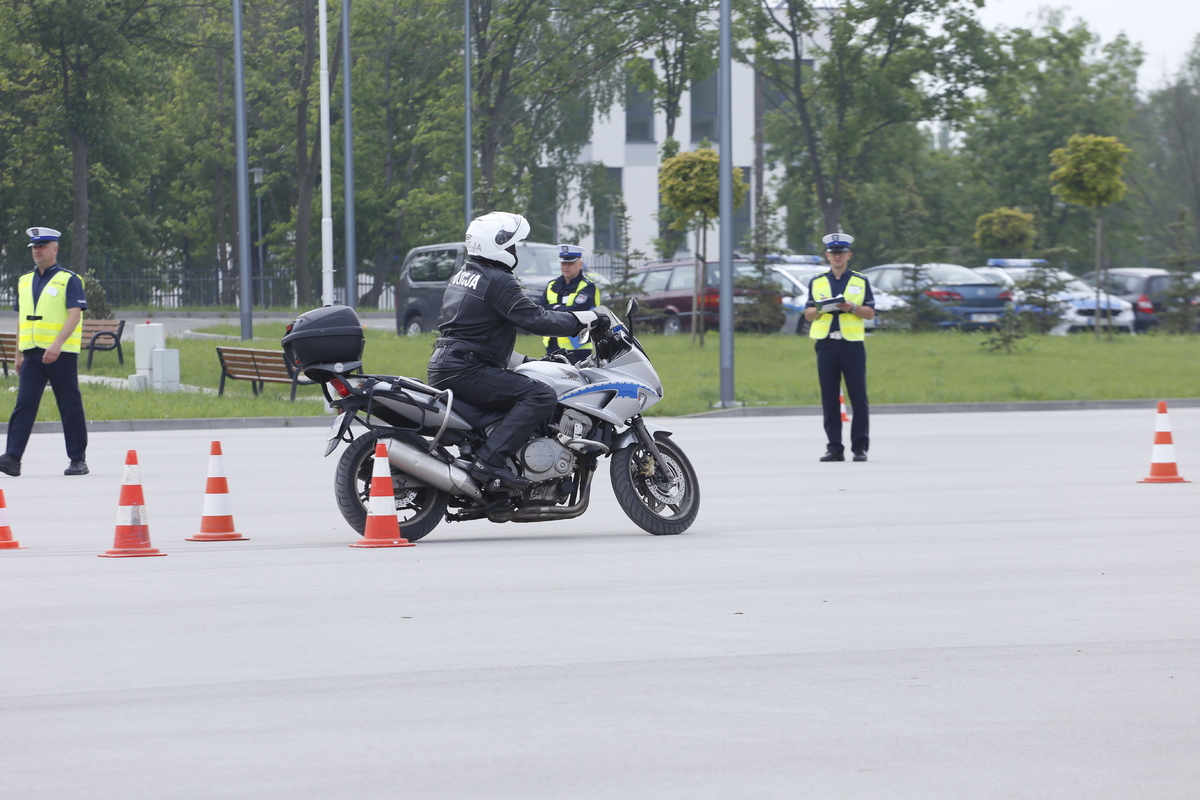 Policjant na motocyklu. W drugim planie zdjęcia sędziowie oceniający jazdę funkcjonariusza.