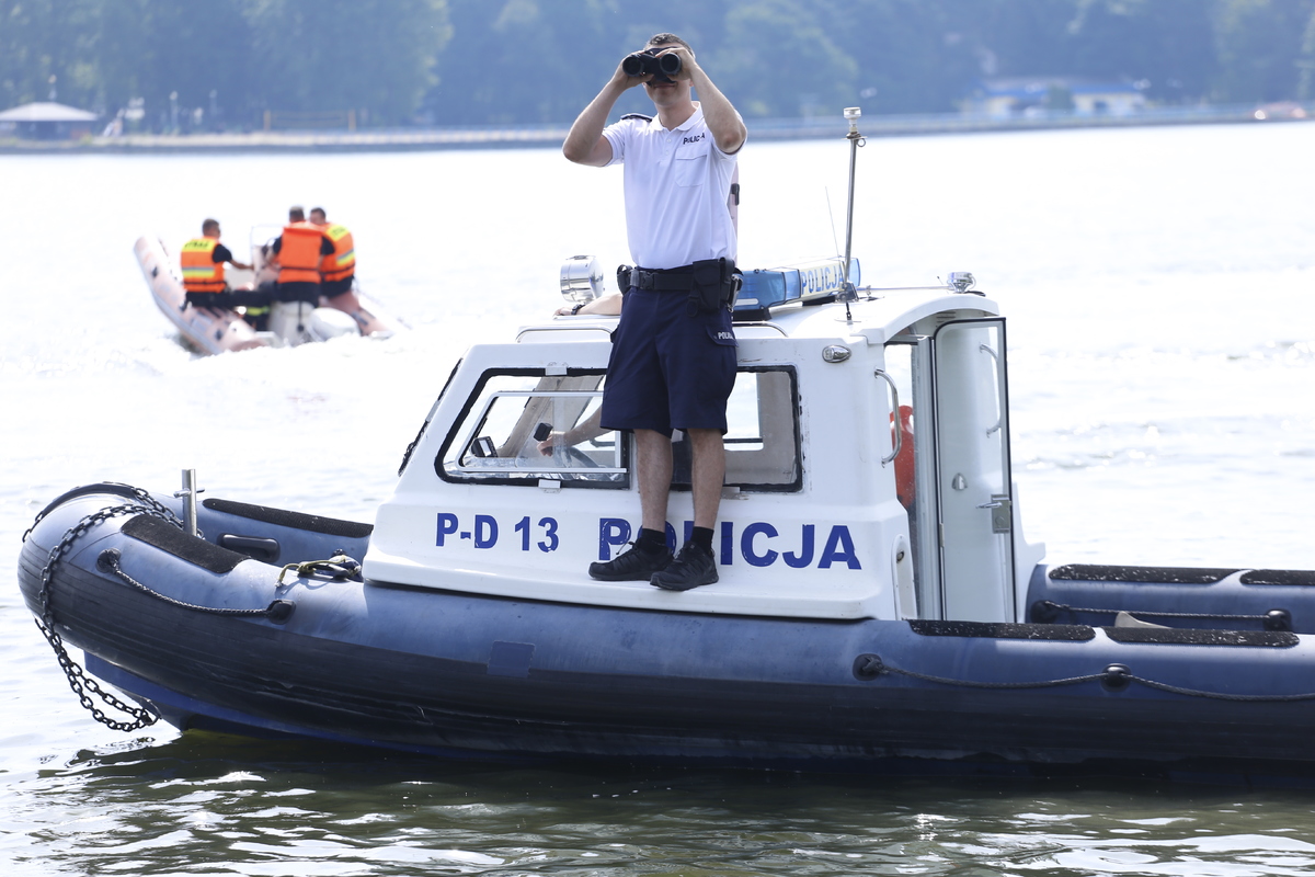 Policjant na łodzi obserwuje akwen wodny przez lornetkę.