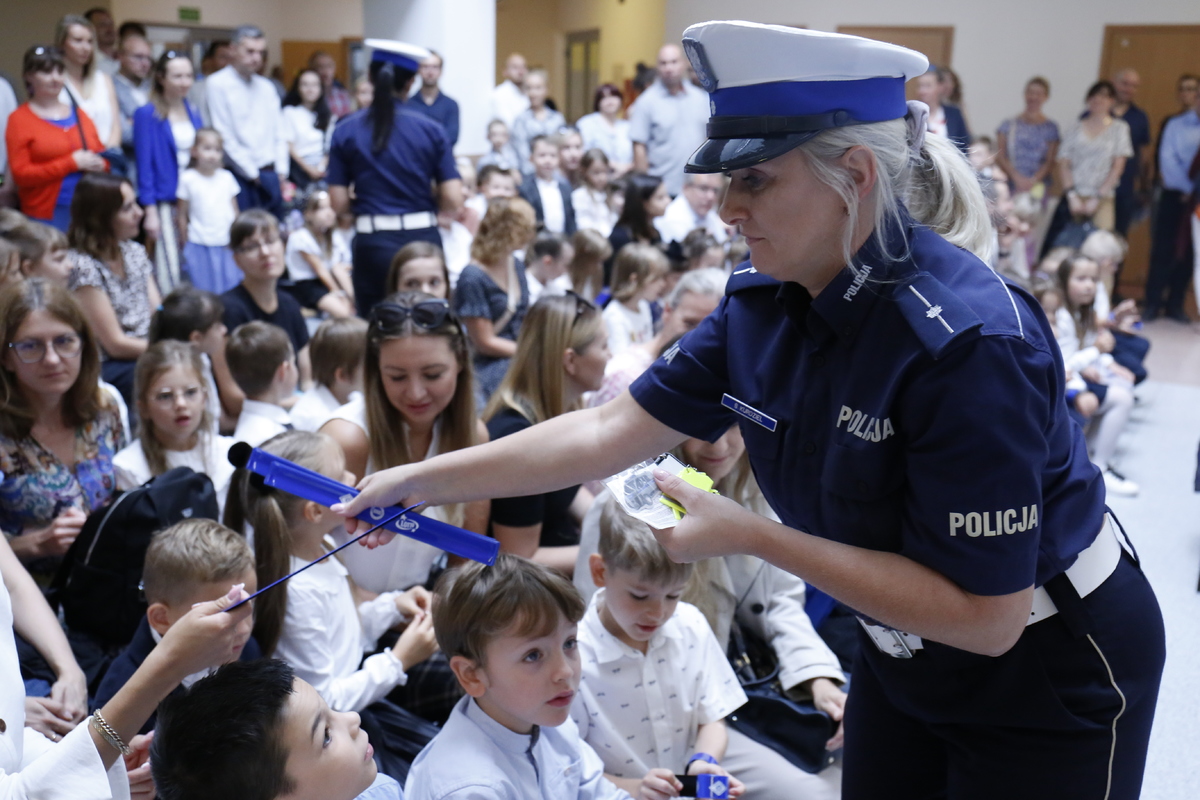 Policjantka rozdjae odblaski dzieciom w szkole.