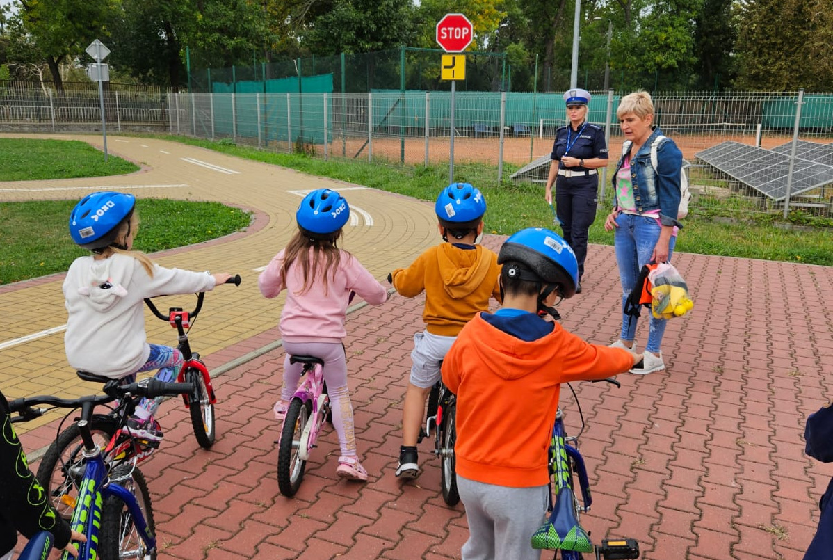 Policjantka tłumaczy dzieciom poruszającym się na rowerach zasady bezpieczeństwa.