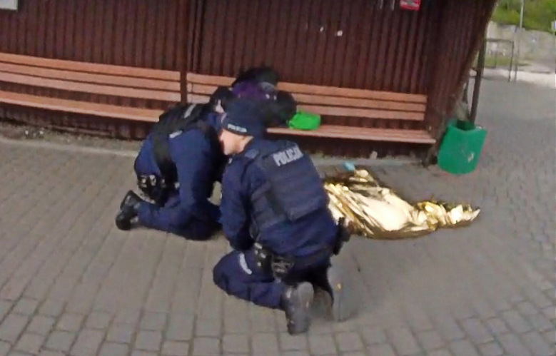 Policjanci prowadzą resuscytację kobiety leżącej na przystanku autobusowym.