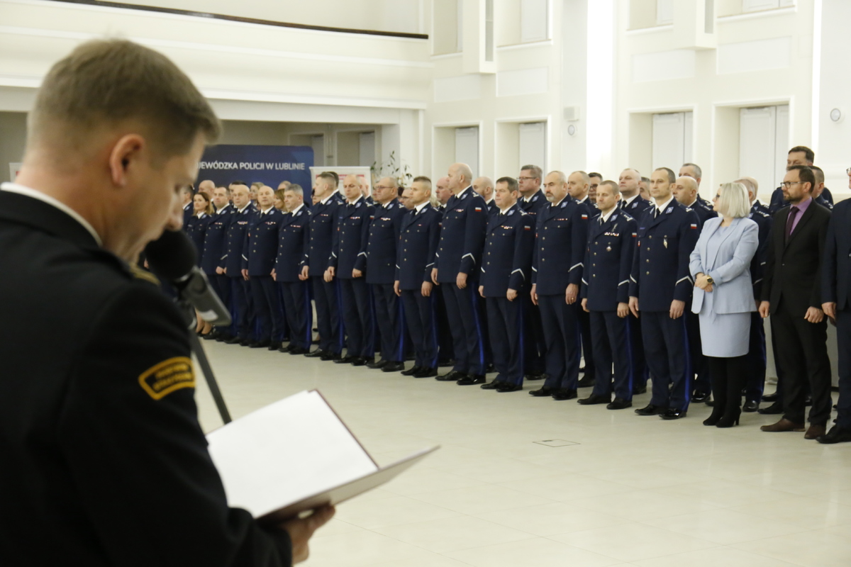 przemawiający Funkcjonariusz Państwowej Straży Pożarnej, na drugim planie znajdują się umundurowani policjanci ustawieni w szeregu.  