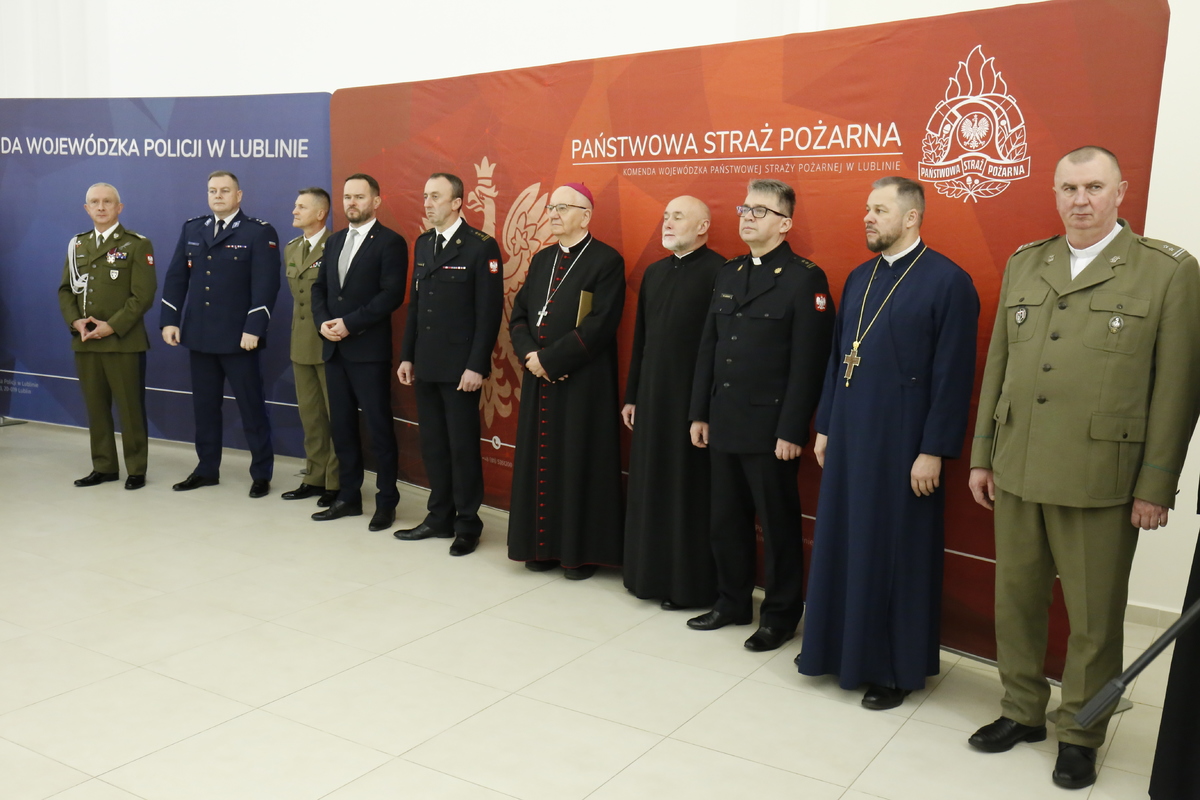 Na tle szyldów Komendy Wojewódzkiej Policji w Lublinie i Państwowej Staży Pożarnej stoją przedstawiciele służb mundurowych województwa lubelskiego oraz duchowni obrządków.