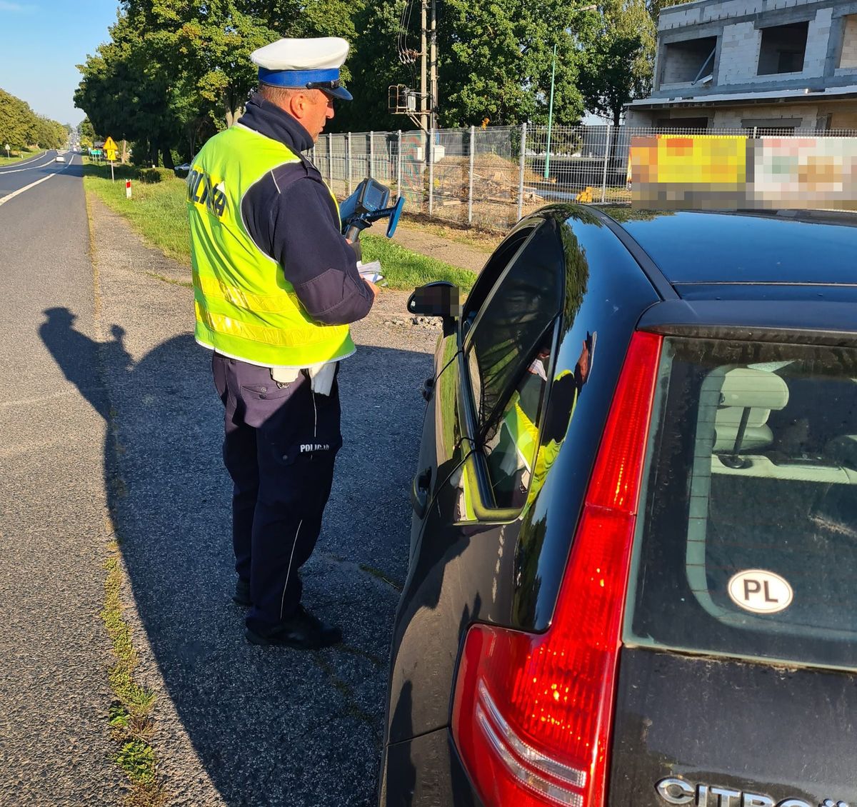 policjant z miernikiem prędkości przy kontrolowanym aucie