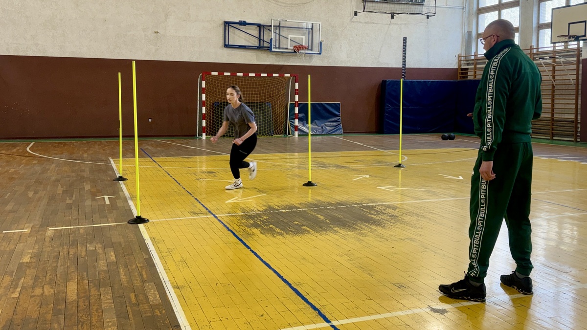 uczennica biega wokół słupków, nieumundurowany policjant liczy czas na stoperze