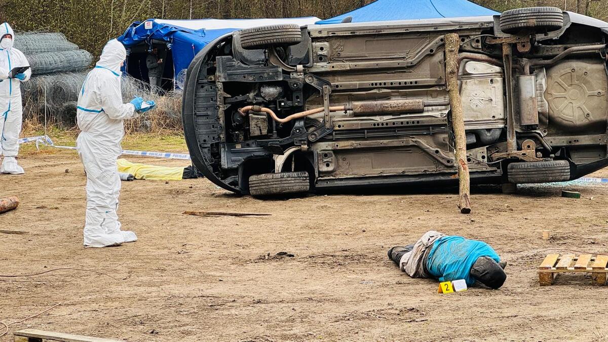 Przewrócone auto osobowe oraz manekin leżący na ziemi.