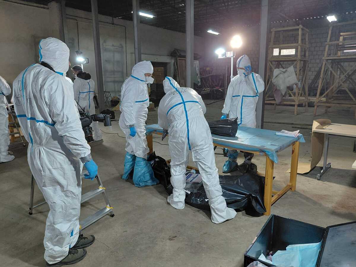 Policjanci ubrani w stroje ochronne w tymczasowym prosektorium poddają dalszym oględzinom szczątki.