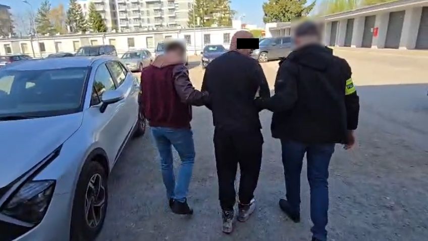 Policjanci prowadzą zatrzymanego mężczyznę.