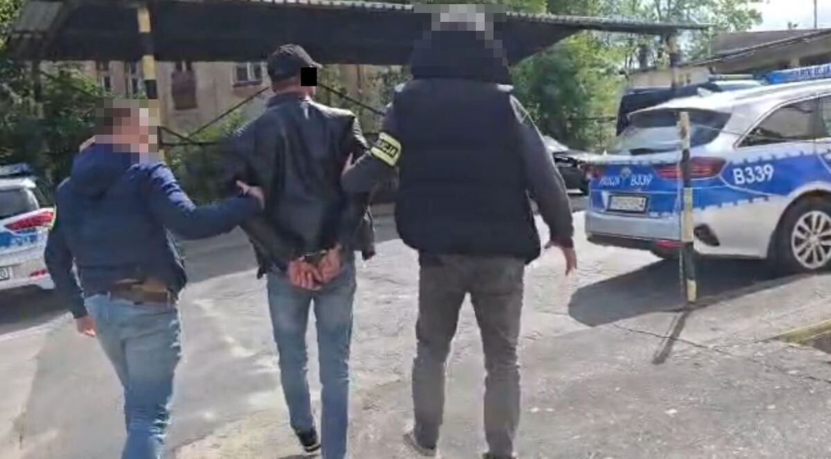 Policjanci prowadzą zatrzymanego poszukiwanego mężczyznę