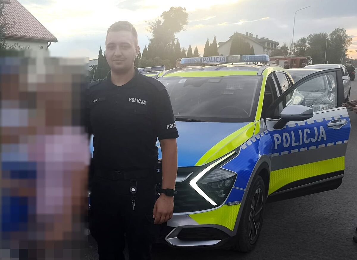 policjant przy radiowozie, obok kobieta z dzieckiem na reku