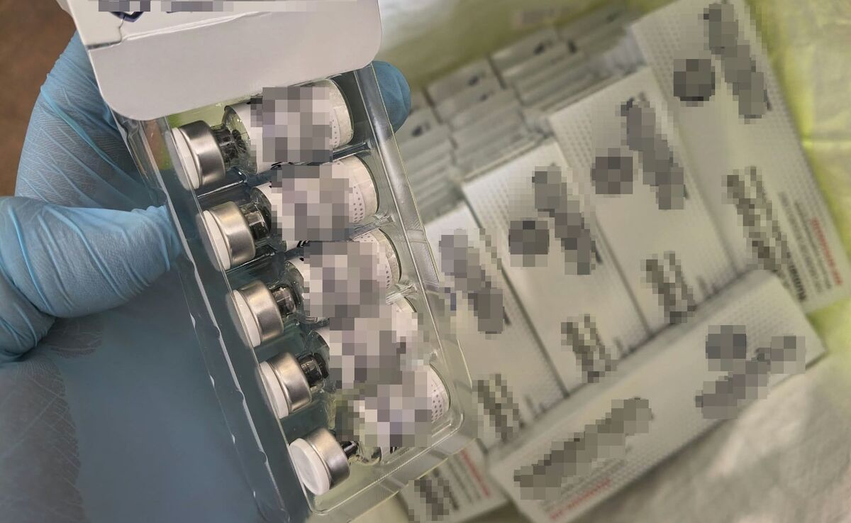 w ręce trzymane opakowanie ze szklanymi fiolkami wypełnionymi płynną substancją, w tle opakowania z wyrobami medycznymi