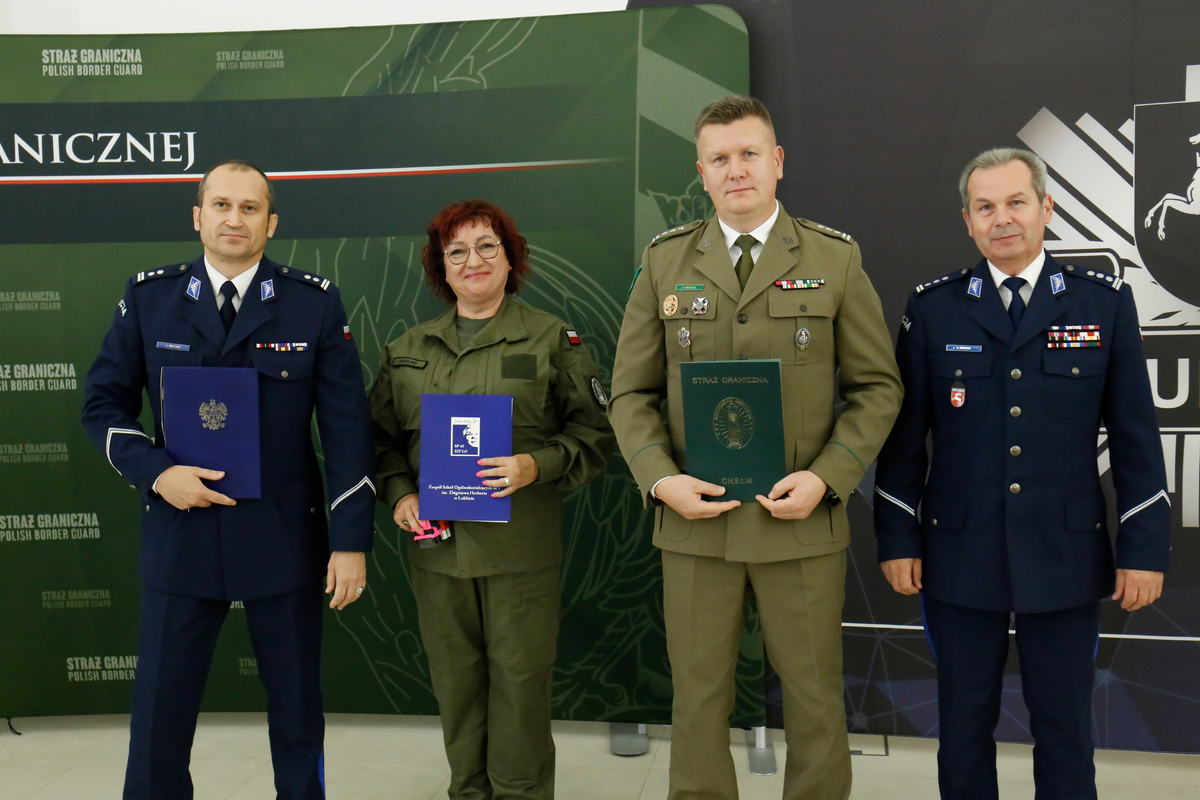 Komendant Miejski Policji w Lublinie młodszy inspektor Adam Beczek, Dyrektor Zespołu Szkół Ogólnokształcących numer 1 imienia Zbigniewa Herberta w Lublinie, Zastępca Komendanta Nadbużańskiego Oddziału Straży Granicznej płk SG Jan Szynal i I zastępca Komendanta Wojewódzkiego Policji w Lublinie inspektro Andrzej Mioduna stoją obok siebie trzymając w dłoniach podpisane porozumienie