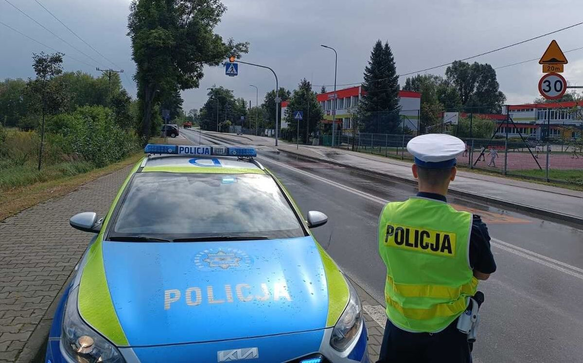 policjant stoi przy radiowozie, w tle jest szkołą