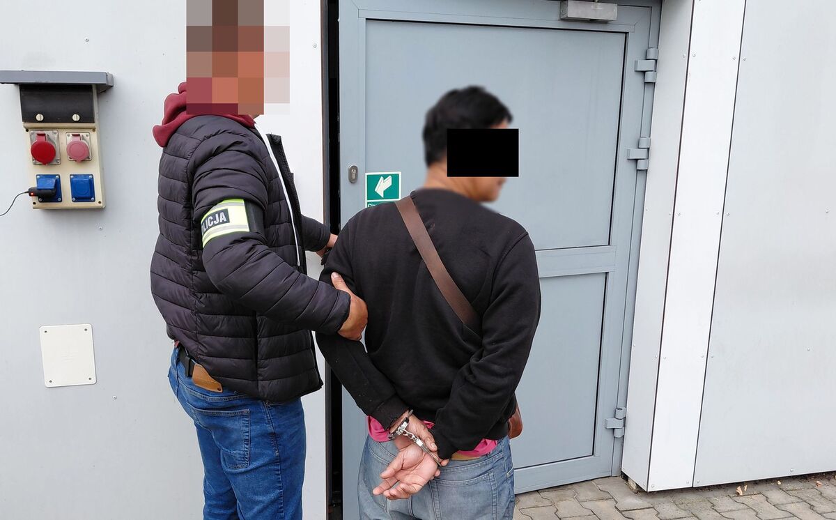 Policjant prowadzi zatrzymanego mężczyznę.