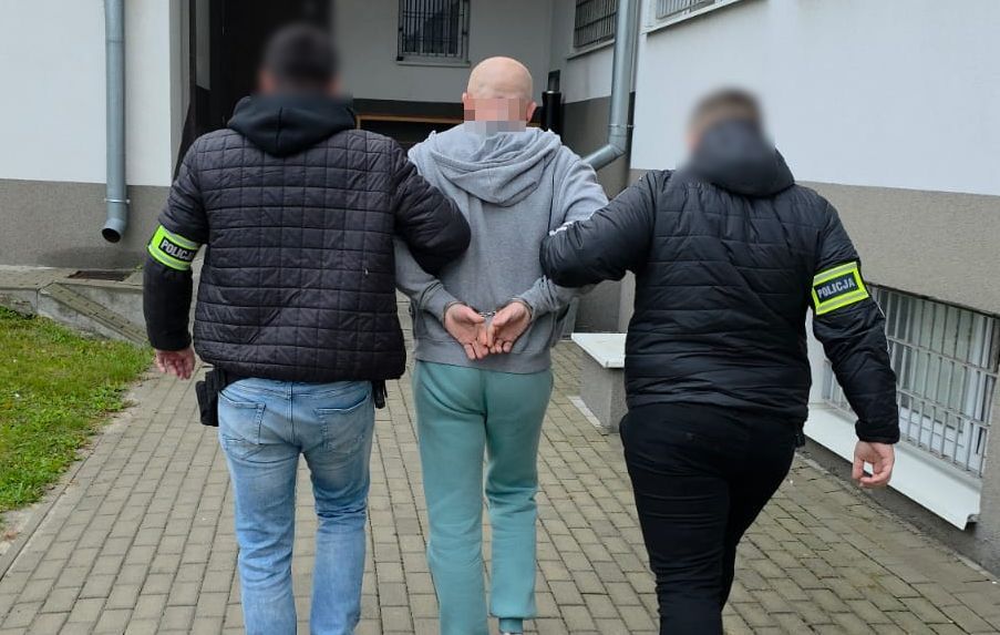 Policjanci prowadzą zatrzymanego mężczyznę.