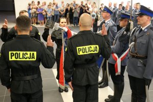 Nowi funkcjonariusze z uniesioną prawą dłonią ślubują na sztandar Komendy Wojewódzkiej Policji w Lubinie.