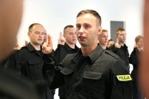Nowi funkcjonariusze z uniesioną prawą dłonią ślubują na sztandar Komendy Wojewódzkiej Policji w Lubinie.