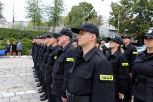 Nowi funkcjonariusze stoją na placu przed Komendą Wojewódzką Policji w Lublinie. Zdjęcie zrobione od strony lewego ramienia funkcjonariuszy.