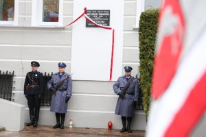 Czterech policjantów stoi na baczność po dwóch stronach tablicy umieszczonej na ścianie Komendy Wojewódzkiej Policji w Lublinie. Dwóch Policjantów jest ubranych w mundury współczesne a dwóch w mundury policji państwowej.