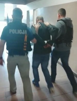 fot. policjanci prowadzą zatrzymanego podpalacza