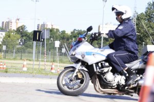 Policjant na motocyklu pokonuje tor przeszkód na placu manewrowym.