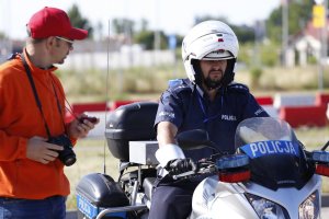 Policjant w kasku siedzi na motocyklu obok sędzia trzyma stoper zwraca się do zawodnika.
