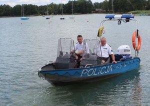 Zdjęcie poglądowe łodzi patrolowej z napisem Policja. Na zdjęciu uwidoczniono dwie sylwetki umundurowanych funkcjonariuszy policji. Łódź znajduje się na tafli Jeziora Białego.
