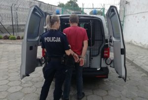 policjantka doprowadza zatrzymanego w tle radiowóz